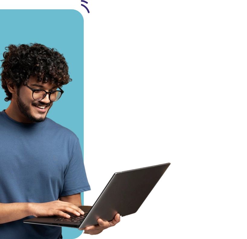 A smiling young man with curly hair and glasses using a laptop, framed against a two-tone blue and grey background